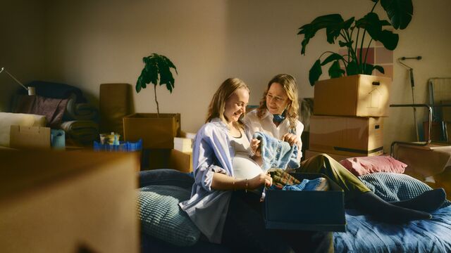 Two women checking baby clothes in a newly moved‑in apartment small